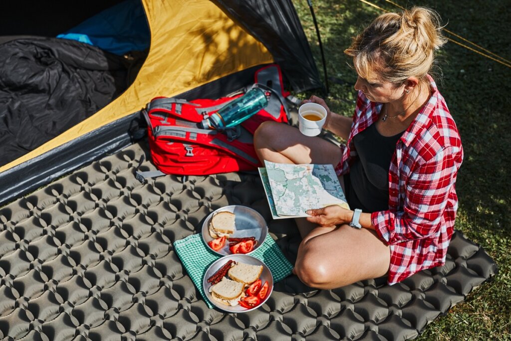 Kobieta na kempingu jedząca śniadanie i czytająca mapę